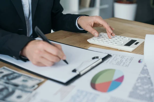 Abgeschnittenes Bild eines Finanziers, der mit Klemmbrett und Taschenrechner im Büro arbeitet — Stockfoto