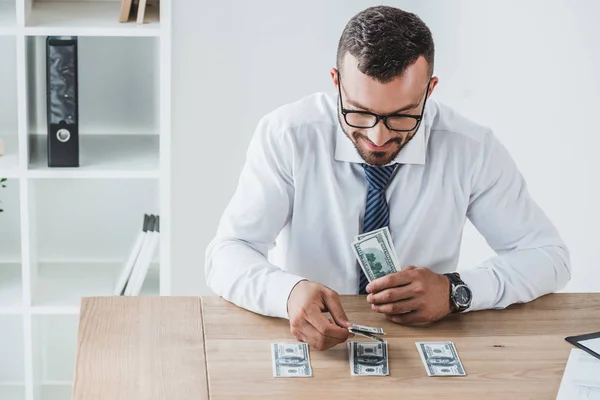 Financiero guapo contando billetes de dólar en la mesa en la oficina - foto de stock