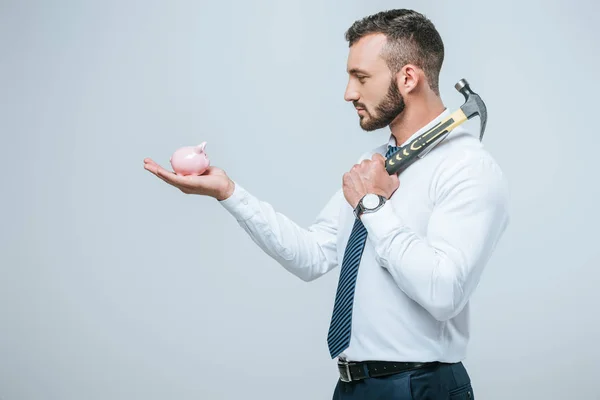 Side view of financier holding piggy bank and hammer isolated on grey — Stock Photo