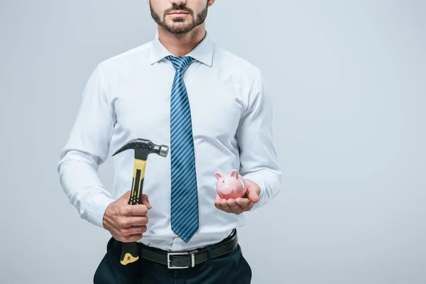 Обрезанное изображение финансиста, стоящего с копилкой и молотком, изолированным на сером — стоковое фото