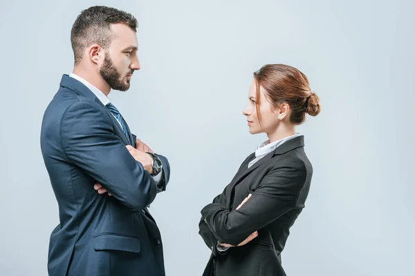 Mujer de negocios y hombre de negocios de pie con los brazos cruzados y mirándose aislados en gris - foto de stock