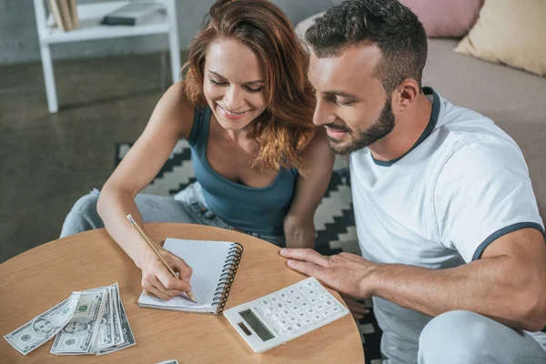 Casal planejando orçamento familiar e escrever algo para notebook na sala de estar — Fotografia de Stock