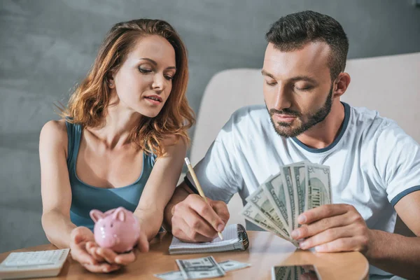 Couple planning family budget with piggy bank and dollars in living room — Stock Photo