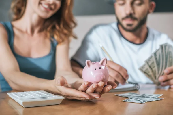 Abgeschnittenes Bild von Paar, das Familienbudget plant und Sparschwein im Wohnzimmer hält — Stockfoto