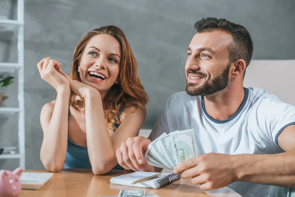 Sonriente pareja planeando presupuesto familiar y mirando hacia otro lado en la sala de estar - foto de stock