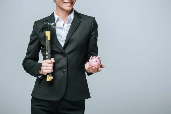 Обрезанное изображение финансиста, держащего молоток и копилку, изолированные на сером — стоковое фото