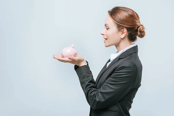 Side view of attractive financier holding piggy bank isolated on grey — Stock Photo