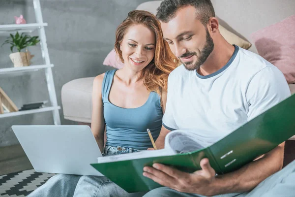 Happy couple planning family budget in living room with laptop and folder — Stock Photo