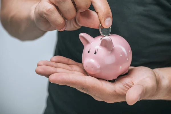 Cropped image of man putting coin in pink piggybank isolated on grey — Stock Photo