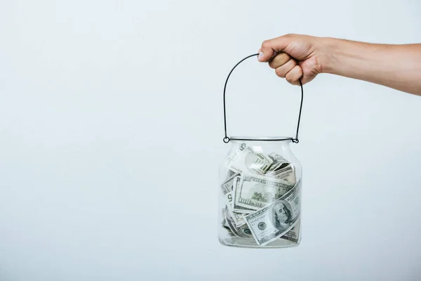 Cropped image of man holding glass jar with dollars isolated on grey — Stock Photo