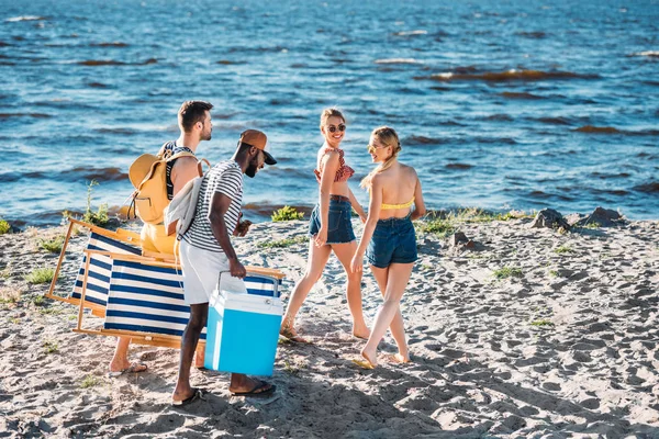 High angle view of young multiethnic friends with beach items walking on sandy sea coast — Stock Photo