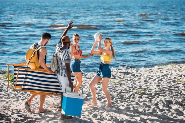 Happy young multiethnic friends with beach items smiling each other on sandy sea coast — Stock Photo