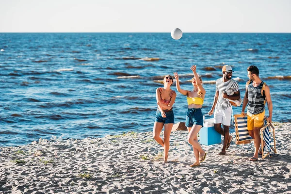 Happy young multiethnic friends playing with ball while walking on sandy beach — Stock Photo