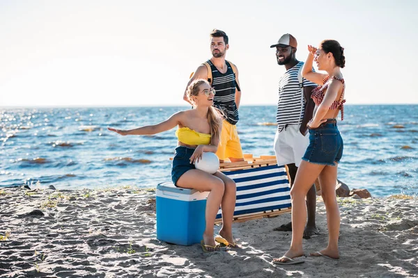 Счастливые молодые люди с пляжными вещами, проводящие время на песчаном побережье моря — стоковое фото