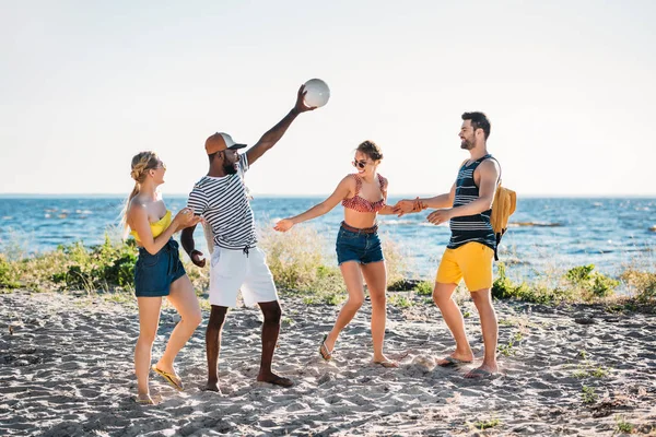 Счастливые молодые люди, играющие с мячом на песчаном пляже — стоковое фото