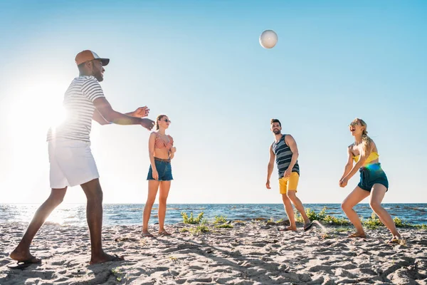 Felices jóvenes amigos multiétnicos jugando voleibol en la playa de arena - foto de stock