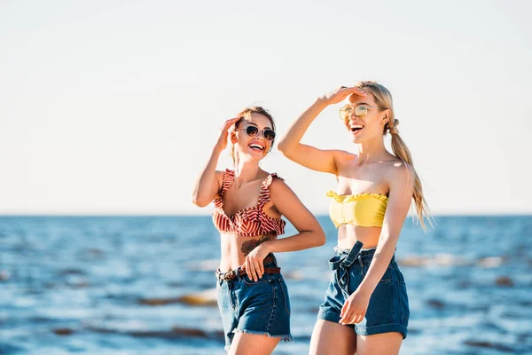 Glückliche junge Frauen mit Sonnenbrille, die gemeinsam am Strand spazieren gehen — Stockfoto