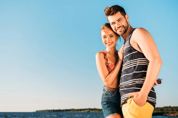 Schönes glückliches junges Paar lächelt in die Kamera, während es zusammen am Strand steht — Stockfoto