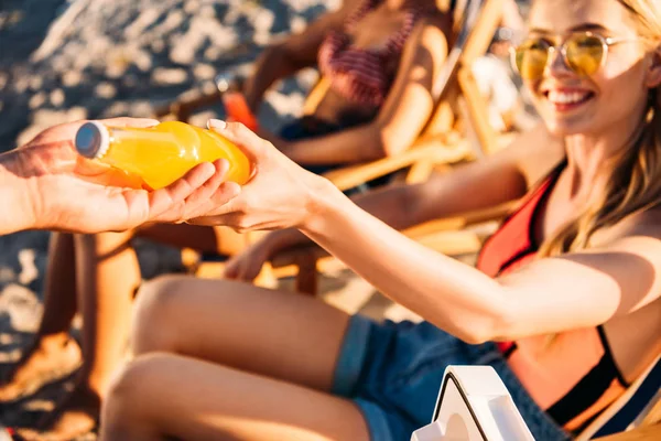 Colpo ritagliato di uomo che dà bottiglia di bevanda estiva alla donna felice sulla spiaggia — Foto stock