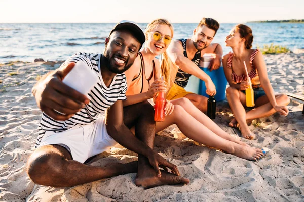 Счастливые молодые люди из разных этнических групп делают селфи со смартфоном, проводя время вместе на песчаном пляже — стоковое фото