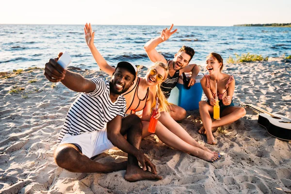 Happy young multiethnic friends taking selfie with smartphone on sandy beach — Stock Photo