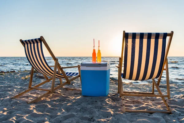 Refreshing beverages on cooler and chaise lounges on sandy beach at sunset — Stock Photo