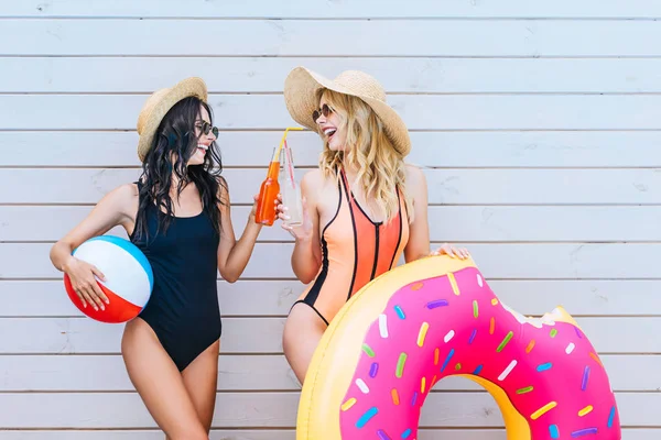 Красиві усміхнені дівчата смердять пляшки з освіжаючими напоями і тримають пляжні предмети біля басейну — стокове фото