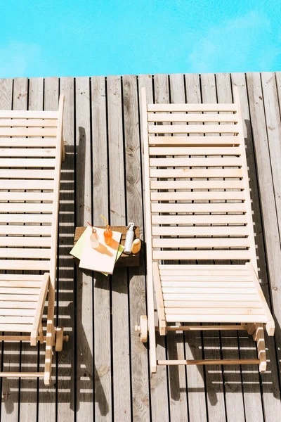 Vista de ángulo alto de las tumbonas vacías y botellas con bebidas de verano cerca de la piscina - foto de stock