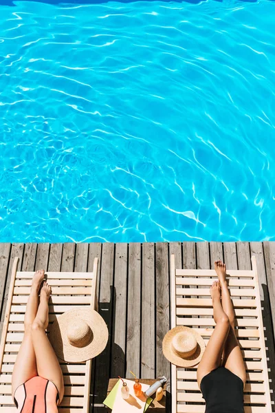 Cropped shot of young women in swimwear resting on chaise lounges near swimming pool — Stock Photo