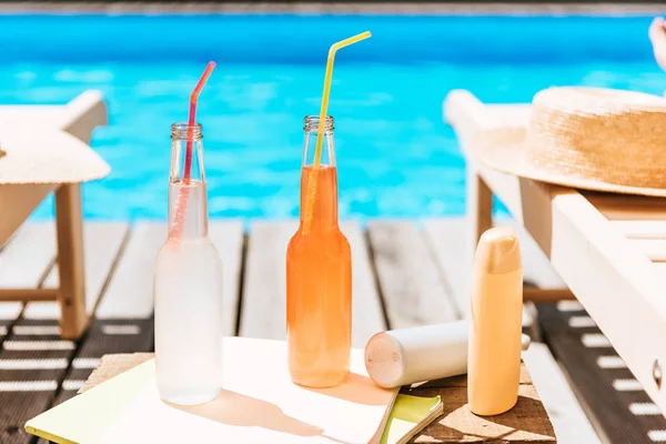 Vista de perto de garrafas com bebidas de verão, protetor solar e salões de chaise na piscina — Fotografia de Stock