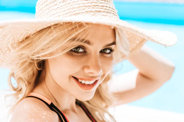 Retrato de hermosa joven rubia en sombrero de mimbre sonriendo a la cámara cerca de la piscina - foto de stock