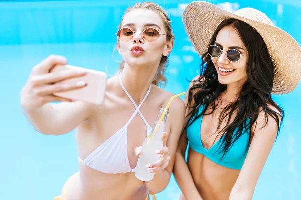 Beautiful happy young women in swimwear taking selfie with smartphone near swimming pool — Stock Photo