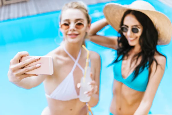 Hermosas novias jóvenes tomando selfie con teléfono inteligente en la piscina - foto de stock