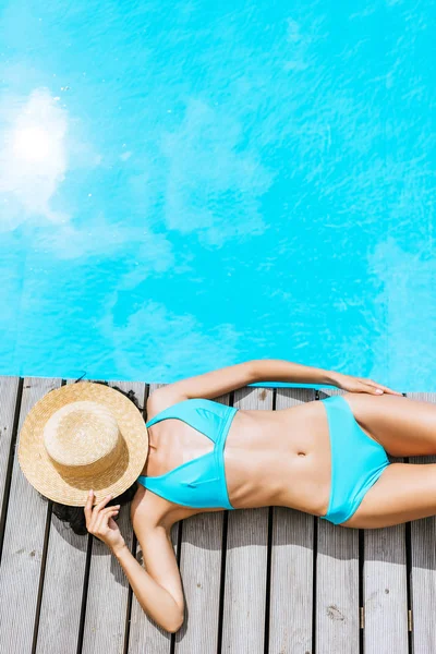 Top view of young woman in bikini and straw hat on face lying near swimming pool — Stock Photo