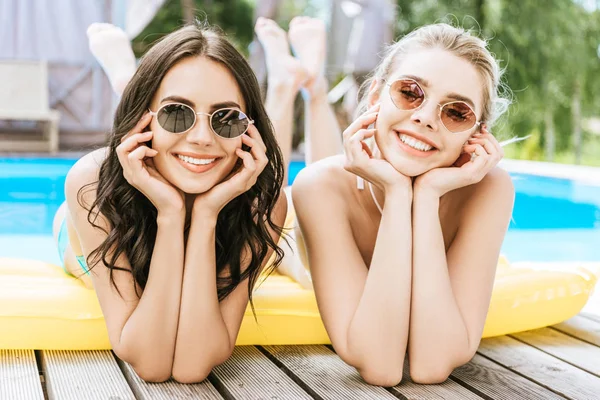 Belle giovani donne sdraiate sul materasso gonfiabile e sorridenti alla fotocamera a bordo piscina — Foto stock