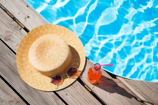 Вид зверху на плетений капелюх, сонцезахисні окуляри та пляшку з літнім напоєм біля басейну — стокове фото