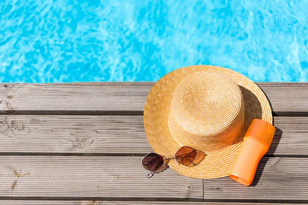 Vista superior del sombrero de mimbre, gafas de sol y protector solar cerca de la piscina - foto de stock