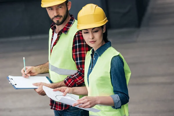 Ingenieure in Hardhats arbeiten mit Bauplan und Klemmbrett auf dem Dach — Stockfoto