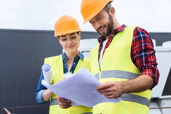 Constructores profesionales en sombreros de trabajo con planos en el techo - foto de stock