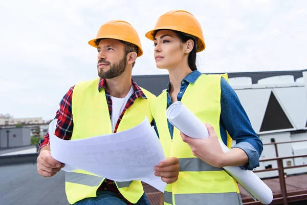 Male and female architects working with blueprints on roof — Stock Photo