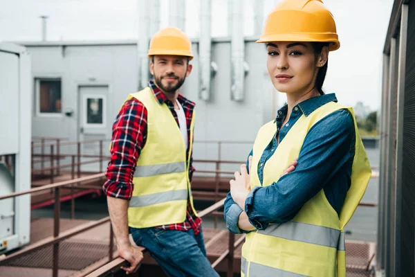 Professionelle Architekten in Warnwesten und Helmen posieren auf dem Dach — Stockfoto