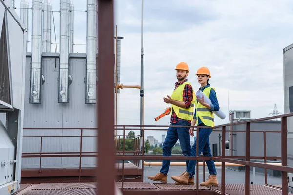 Professional architects in helmets with blueprint and level walking on roof — Stock Photo