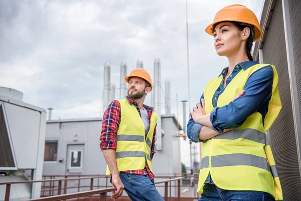 Professional engineers in safety vests and helmets posing on roof — Stock Photo