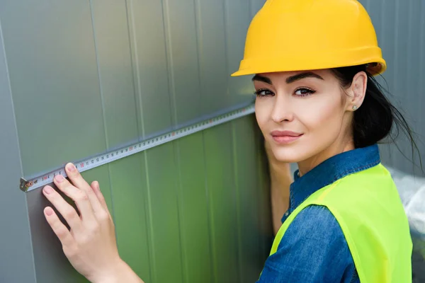 Female architect in hardhat measuring metal wall — Stock Photo