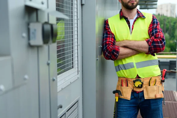 Cropped view of engineer in safety vest with tool belt posing with crossed arms — Stock Photo