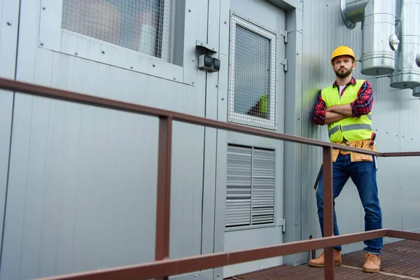 Männlicher Berufsarchitekt in Sicherheitsweste posiert mit verschränkten Armen auf der Baustelle — Stockfoto