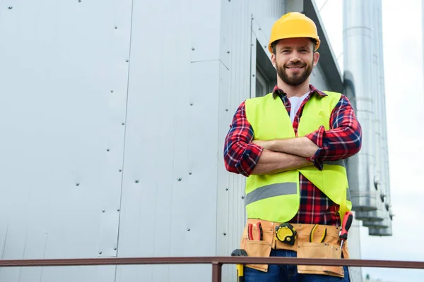 Männlicher Berufsingenieur mit Werkzeuggurt posiert mit verschränkten Armen — Stockfoto