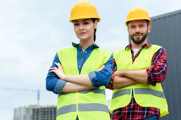 Professional architects posing in helmets and safety vests with crossed arms — Stock Photo