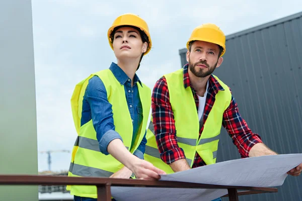 Professional engineers in helmets working with blueprints and looking on construction — Stock Photo