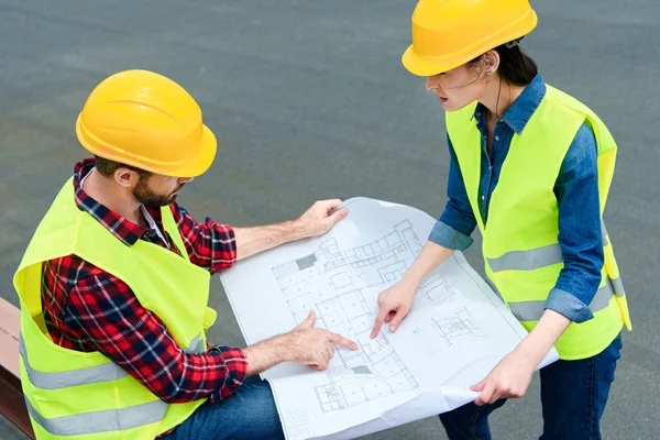 Construct colleagues in safety vests and helmets working with blueprint — Stock Photo